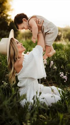 a woman holding a baby up in the air while sitting on her stomach and wearing a hat