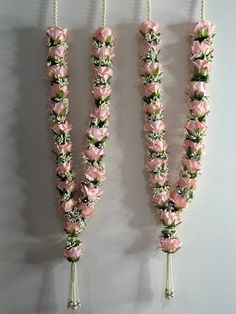 three pink flowers are attached to the side of a white wall with beads hanging from it