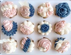 twelve cupcakes decorated with blue, pink and white icing in a box