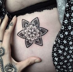 a woman's stomach with a flower tattoo on her belly and hands holding it