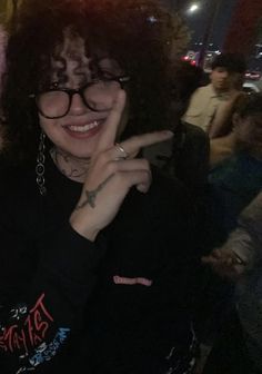 a woman with glasses is smiling and making a peace sign while standing in front of other people