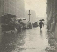 an old black and white photo of people walking down the street in the rain with umbrellas