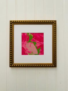 a pink and green painting hanging on a white wall next to a gold framed object