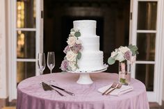 a white wedding cake sitting on top of a table next to wine glasses and utensils