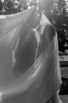 black and white photograph of two people covered by a sheet with trees in the background