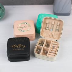 three small boxes with rings and jewelry inside on a table next to a teapot