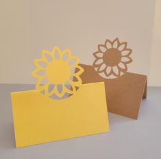 two cards with cut out flowers on them, one yellow and one brown are sitting next to each other