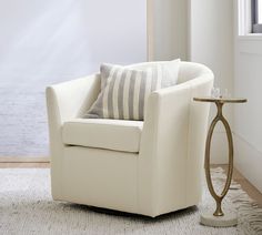 a white chair sitting in front of a window next to a table with a lamp on it