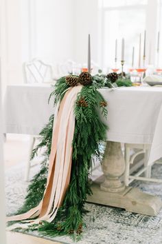 the table is decorated with pine cones, greenery and ribbon as well as candles