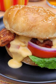 a hamburger with cheese, lettuce and tomato on a black plate next to some drinks