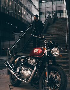 a man standing next to a motorcycle parked on the side of a street near some stairs