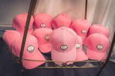 pink baseball caps are stacked on a rack