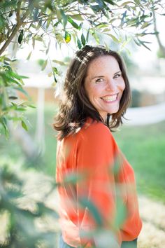 a woman standing under a tree smiling at the camera