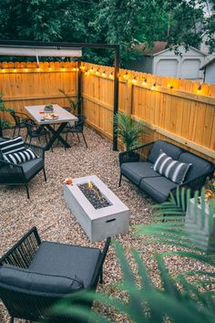 an outdoor seating area with fire pit, chairs and lights on the fence behind it