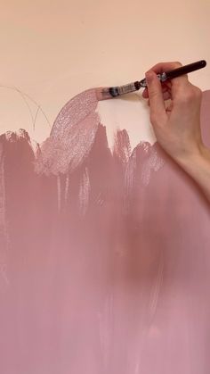 a person is holding a paintbrush and painting the wall with pink colors on it