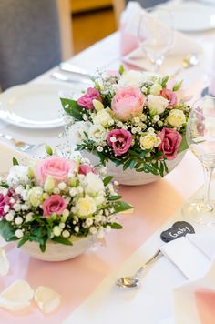 two white bowls with pink and white flowers on a table set for a formal dinner