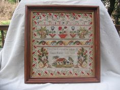 a cross stitch sample is displayed on a white cloth covered chair in front of a wooden frame