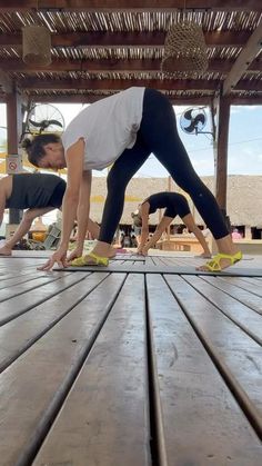 two women doing yoga on wooden planks in an outdoor area with sun shining through the roof