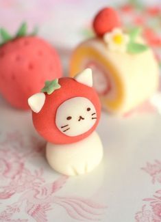 there is a small cat figurine next to two strawberries