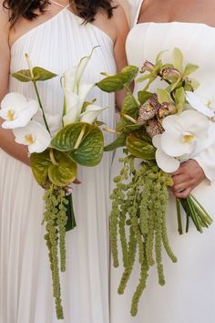 two bridesmaids in white dresses holding bouquets with orchids and greenery