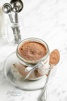 a glass jar filled with cocoa powder on top of a white plate next to two spoons