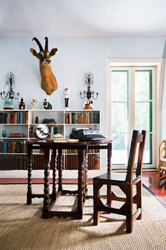 a table with two chairs and a deer head on the wall above it in front of a bookshelf