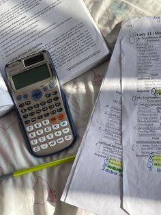 a calculator sitting on top of a bed next to two sheets of paper