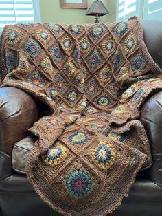 a crocheted blanket sitting on top of a brown couch next to a lamp