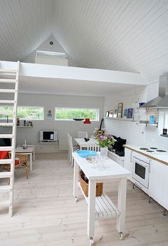 a kitchen with white walls and wooden flooring next to a loft style ceiling fan