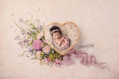 a newborn baby in a heart - shaped basket surrounded by flowers