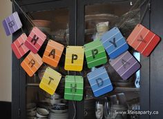 a colorful happy birthday sign hanging from the side of a glass cabinet with dishes on it