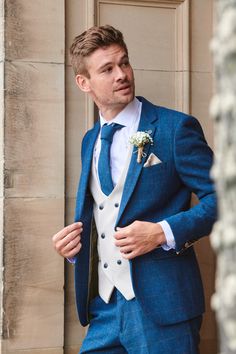 a man in a blue suit and white shirt is standing by a door with his hands in his pockets