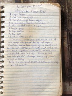 an old notebook with writing on it sitting on top of a wooden table next to a wall