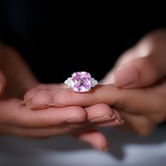 two hands holding a ring with a pink stone in it