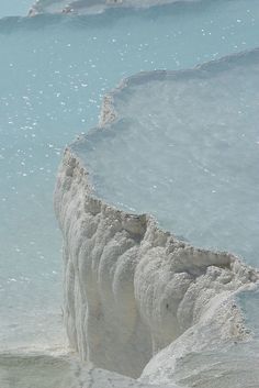 a man standing on the edge of a cliff in front of blue water and ice