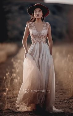 a woman wearing a dress and hat standing in the middle of a dirt field with tall grass