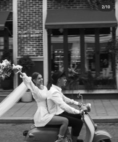 a man and woman riding on the back of a scooter down a street