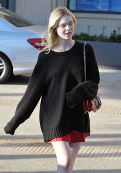 a woman in black sweater and red skirt walking down the street