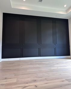 an empty room with black paneling and wood floors in the center is painted white