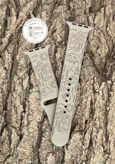 two apple watchbands sitting on top of a tree trunk with graffiti written on them