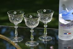 three wine glasses sitting on top of a glass table next to a bottle of grey goose vodka