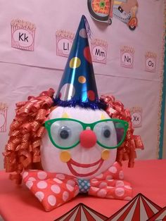 a clown wearing glasses and a party hat on top of a table in front of a wall