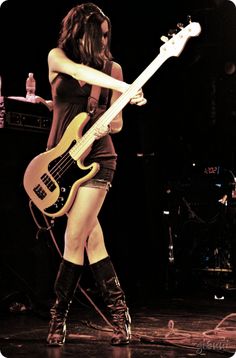 a woman in short shorts and boots holding a bass guitar while standing on a stage