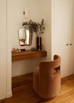 a room with a chair, mirror and plant on the wall next to a desk