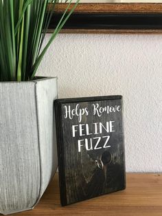 a plant in a white vase next to a sign that says happy remove feline fuzz