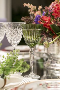 two wine glasses sitting on top of a table with flowers in the background and place settings