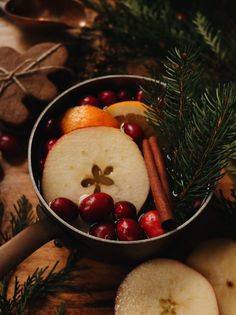 apples, cinnamons and oranges are arranged in a metal bowl on a wooden table