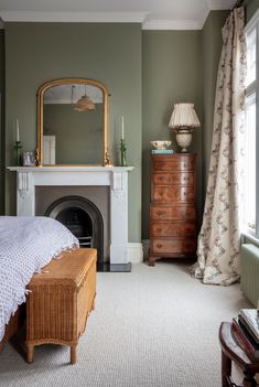 a bedroom with a fireplace, dresser and mirror in it's corner next to a window