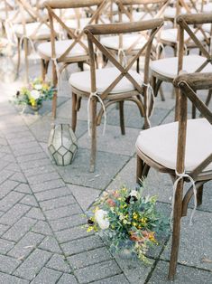 rows of wooden chairs with white cushions and flowers on the ground in front of them