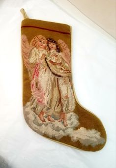 a cross stitch christmas stocking with two angels hugging on it's side, hanging from a cord